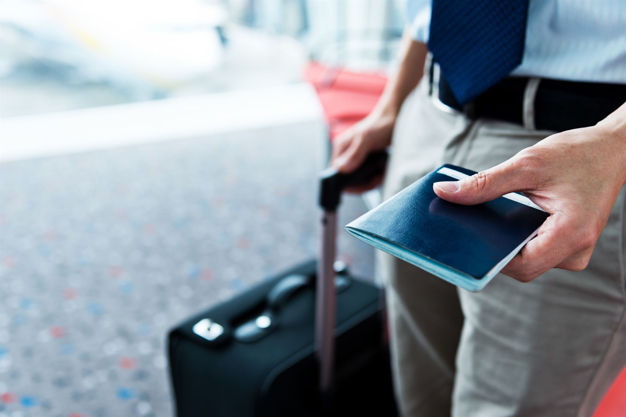 Man-in-business-wear,-standing-with-carry-on-bag,-holding-passport